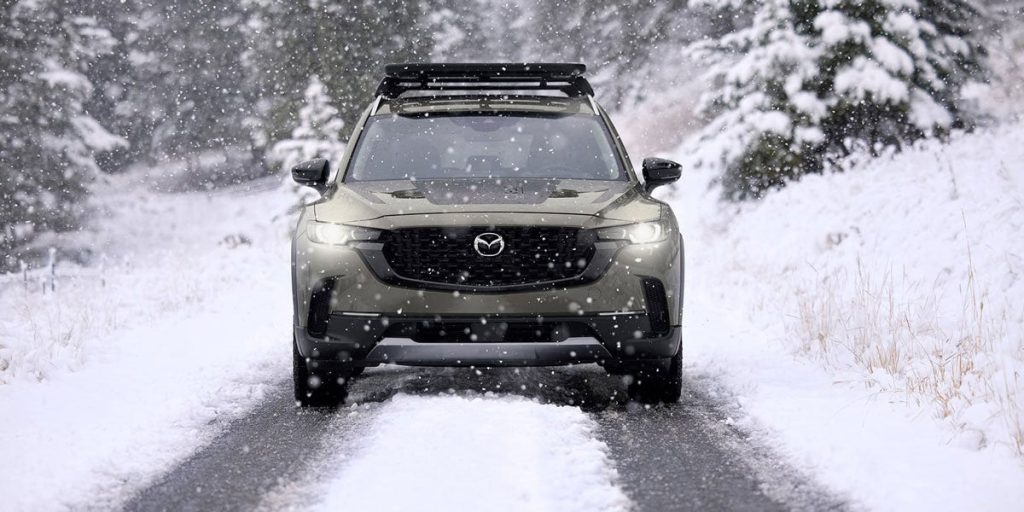 An image of a Mazda CX-50 confidently blazing a trail through the snow, facing directly towards the camera. 