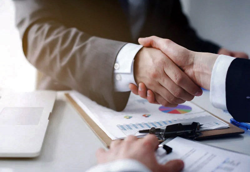 An image of a customer shaking hands with a car dealership finance agent over a new car deal.
