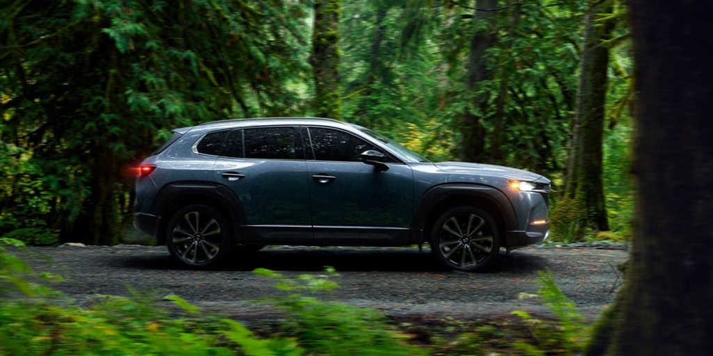 An image of a blue-gray Mazda CX-50 Performance Turbo model driving through the woods.