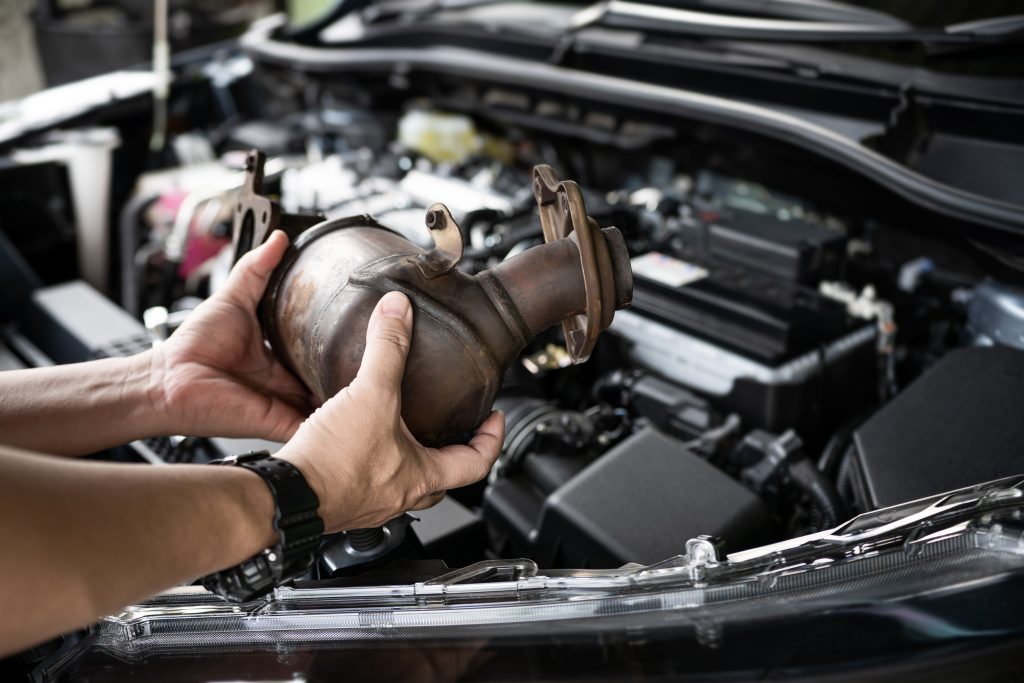 An image of a catalytic converter being held over an engine by a professional technician. 