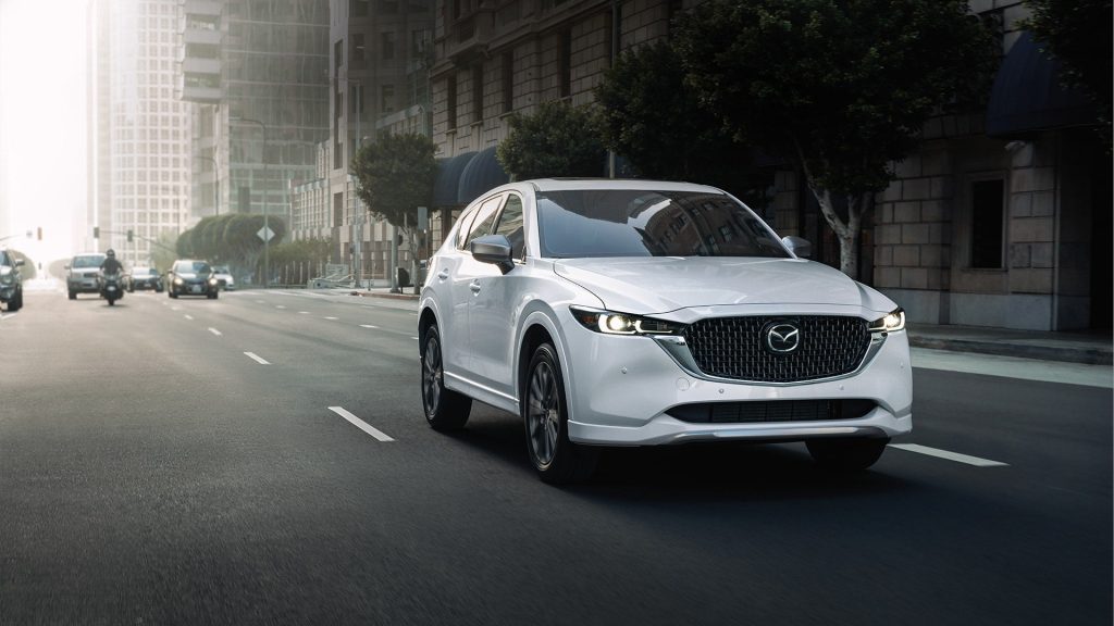 A white 2024 Mazda CX-5 driving down a city street