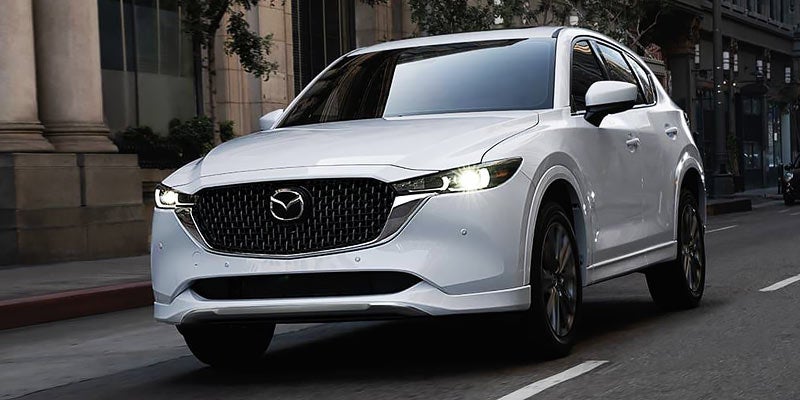 A pearl white Mazda CX-5 driving towards the camera down a city street.