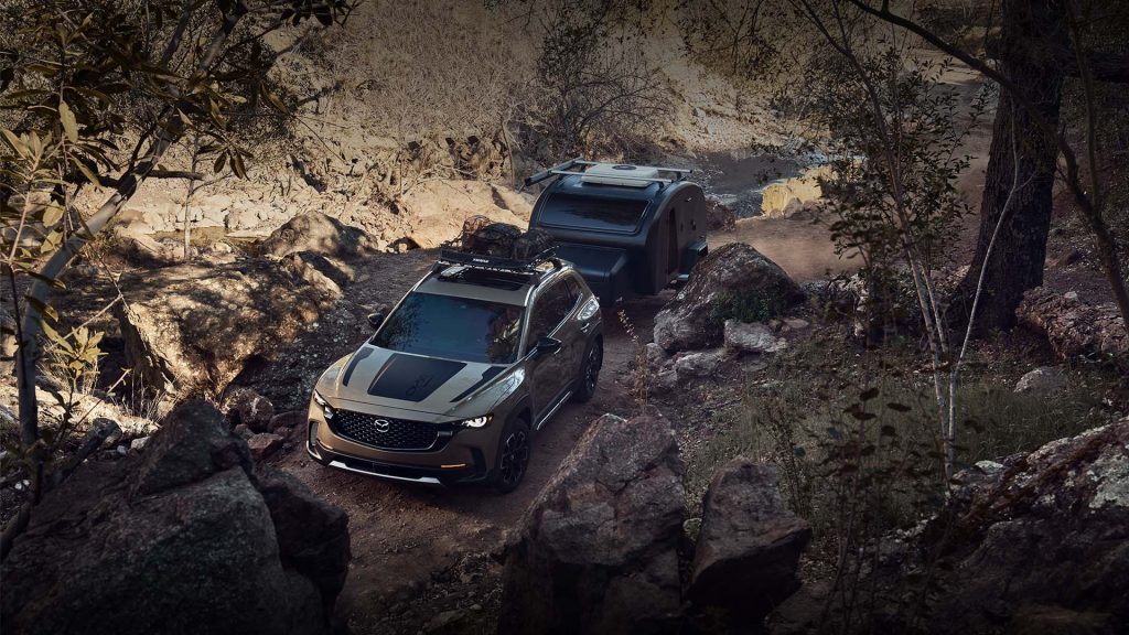 A Mazda CX-50 towing a camping trailer through rocky terrain
