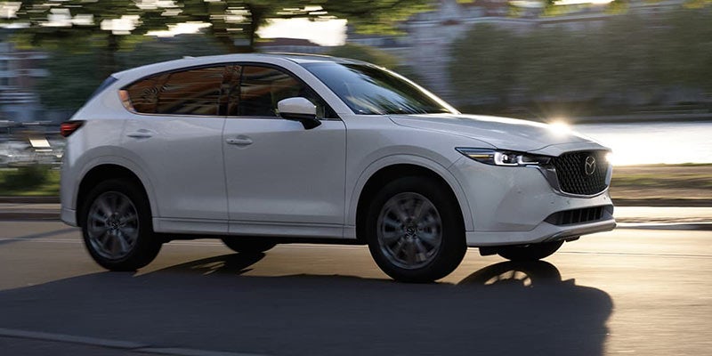 A white 2024 Mazda CX-5 driving down a sunny road.