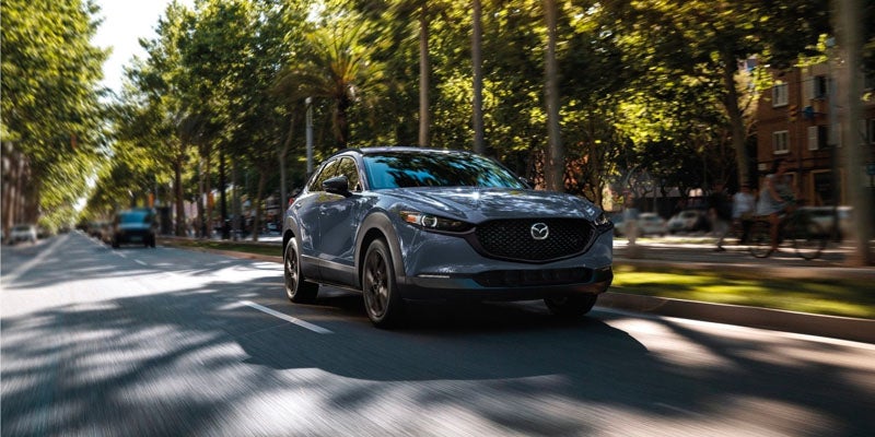 A gray 2025 Mazda CX-30 driving along a tree-lined lane.