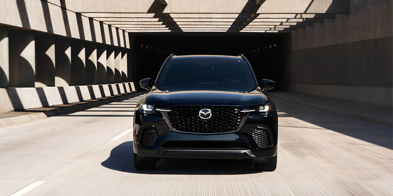 A Mazda CX-70, black, facing the camera on a city street. 