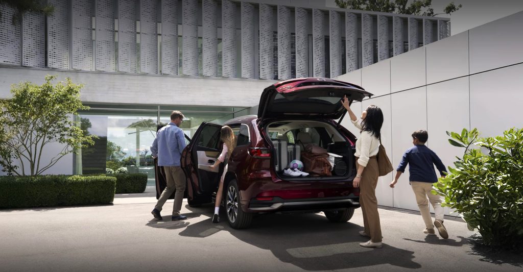 Family loading luggage into a red SUV with open trunk outside a modern home