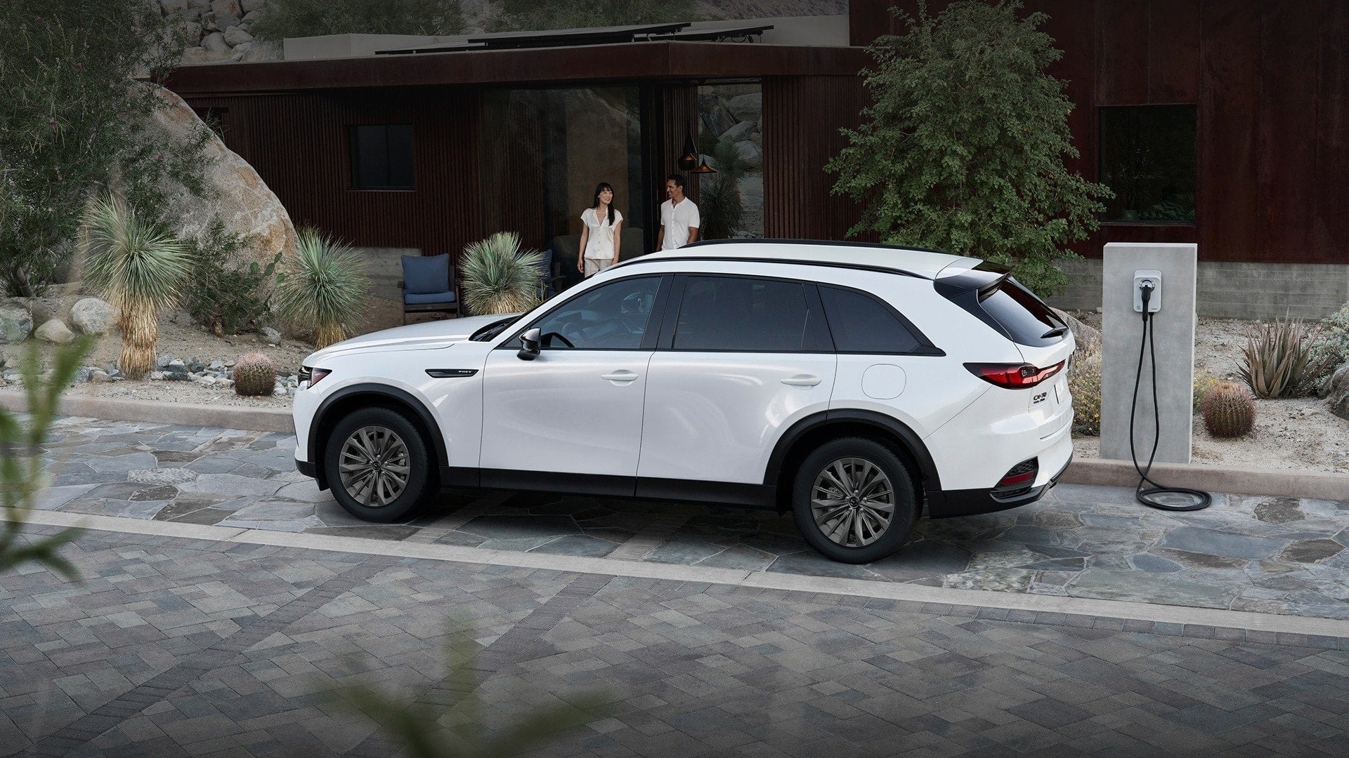 White Mazda SUV connected to a home charging station outside a modern house.