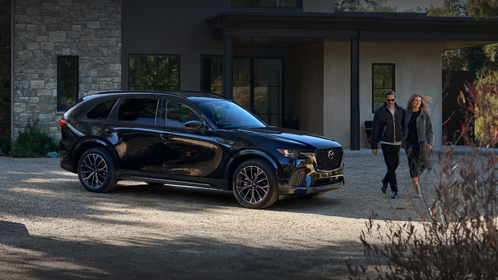 Black Mazda SUV parked outside a modern home with a couple walking nearby.