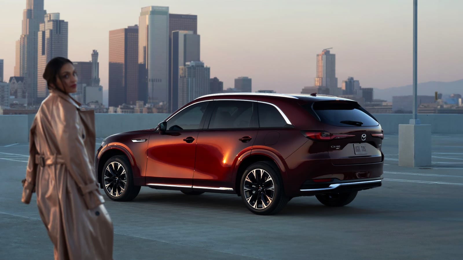 Red Mazda SUV parked along a waterfront with a city skyline in the background.