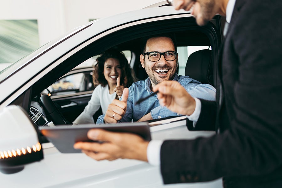 A man smiling in a car while speaking with a salesperson while trading a car.